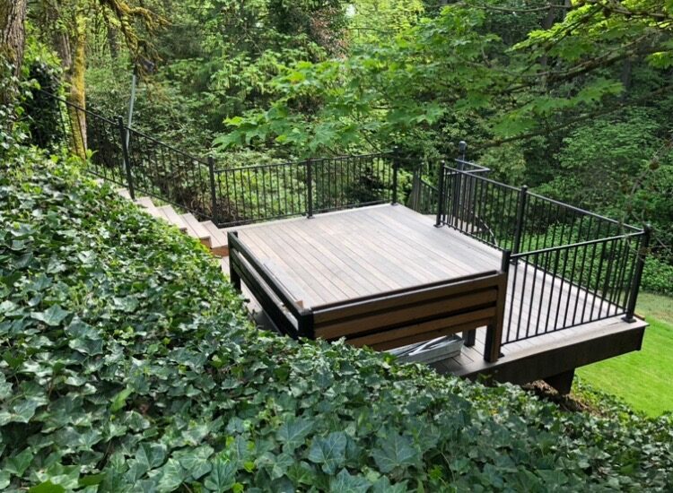 Composite deck with black metal railing surrounded by ivy and mature trees